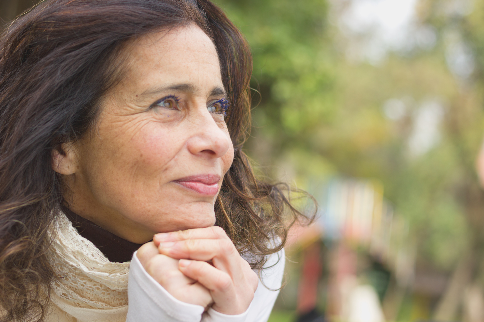 Middle aged nice lady with optimistic look resting face on her hands in the park